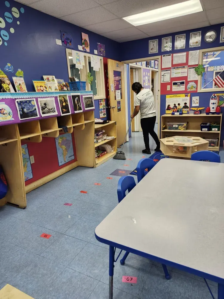 A man is sweeping the floor in a classroom with tables and chairs