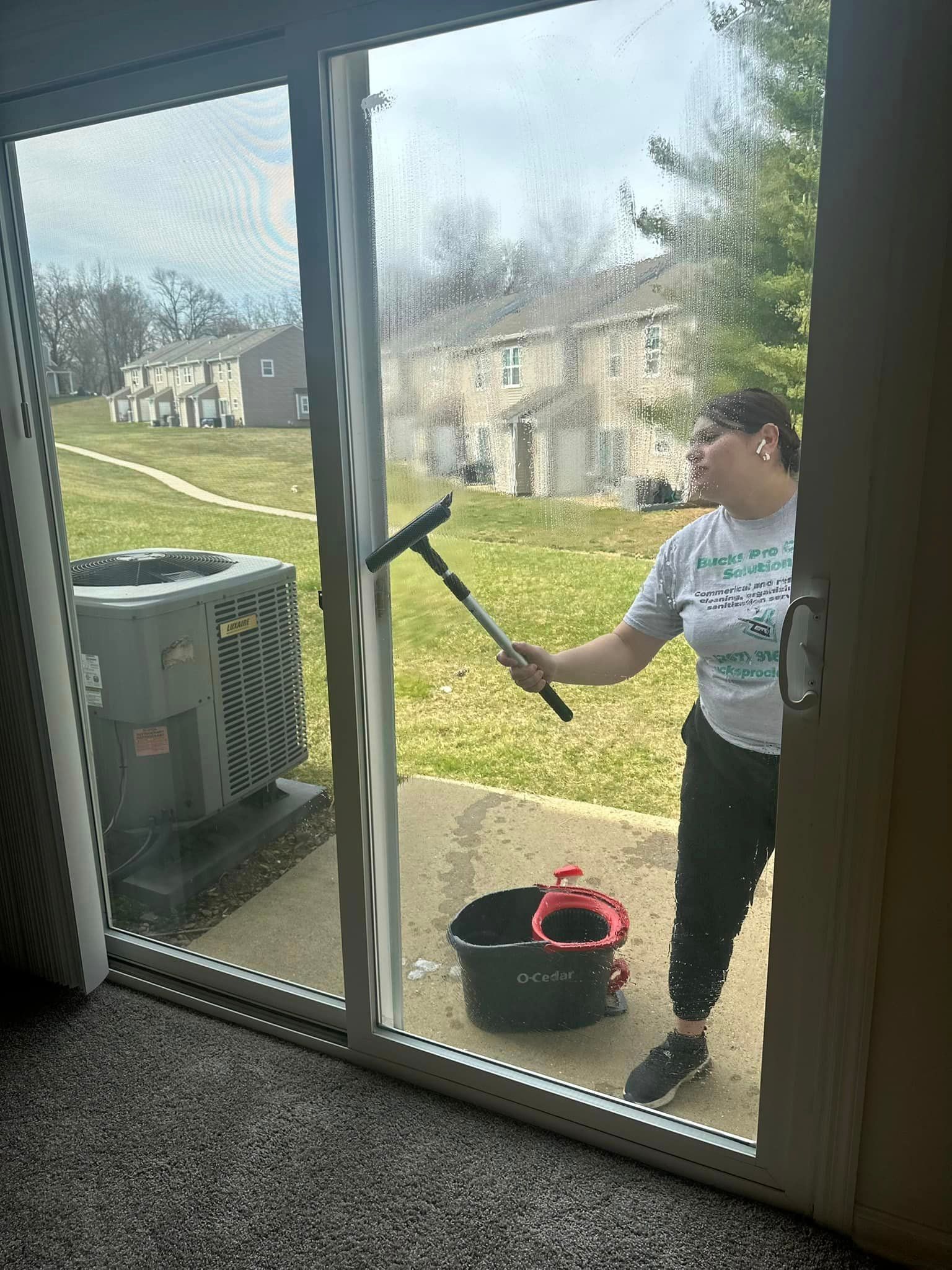 A woman is cleaning a sliding glass door with a mop.