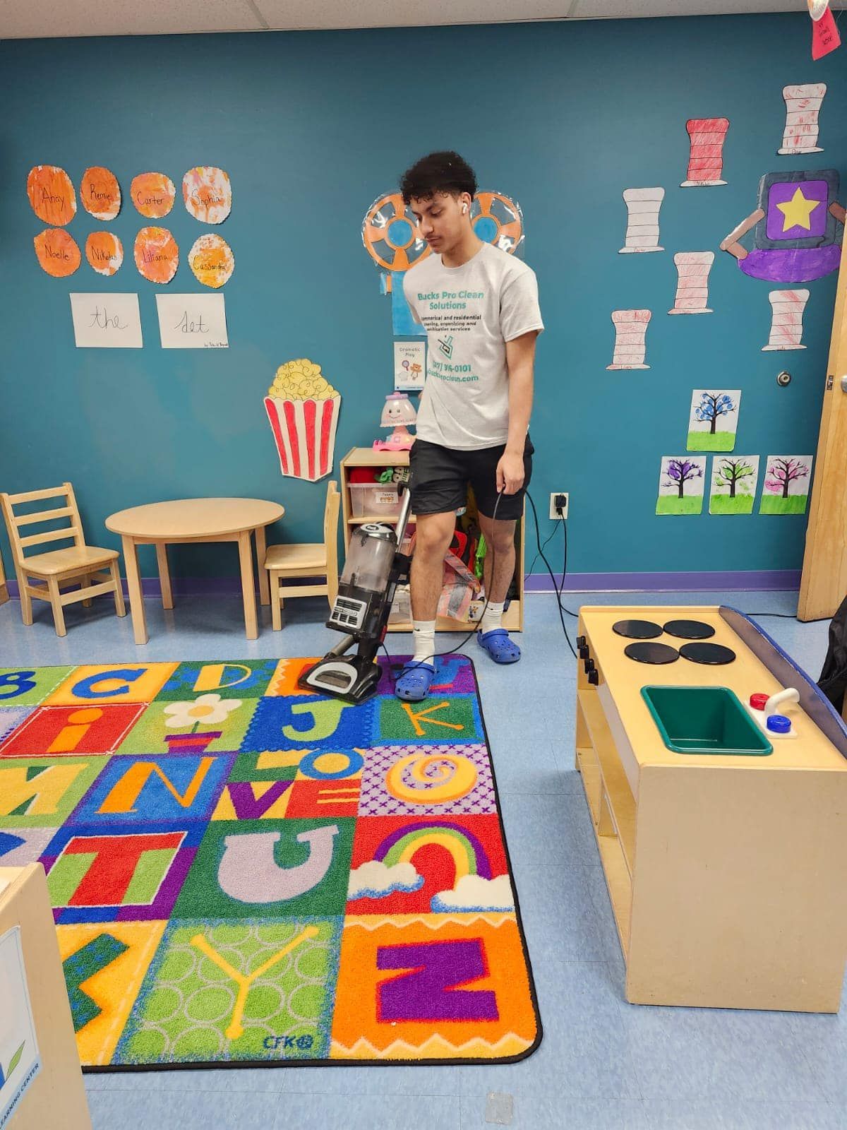 A boy is standing on a rug in a room with a vacuum cleaner.