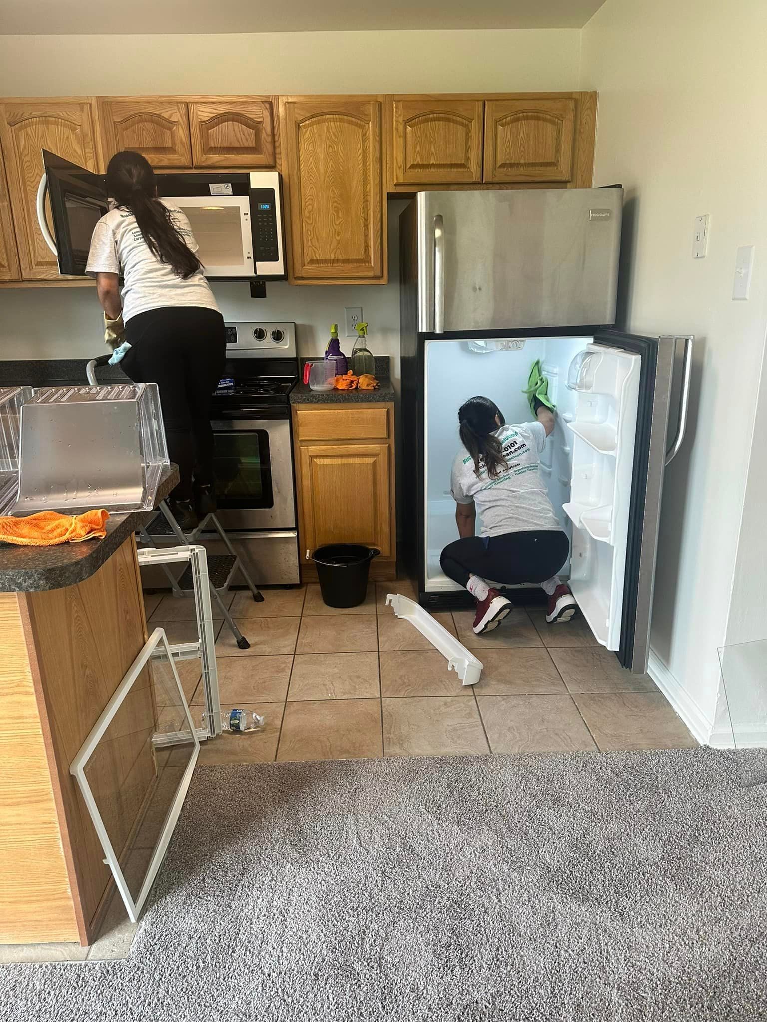 A woman is cleaning the inside of a refrigerator in a kitchen.
