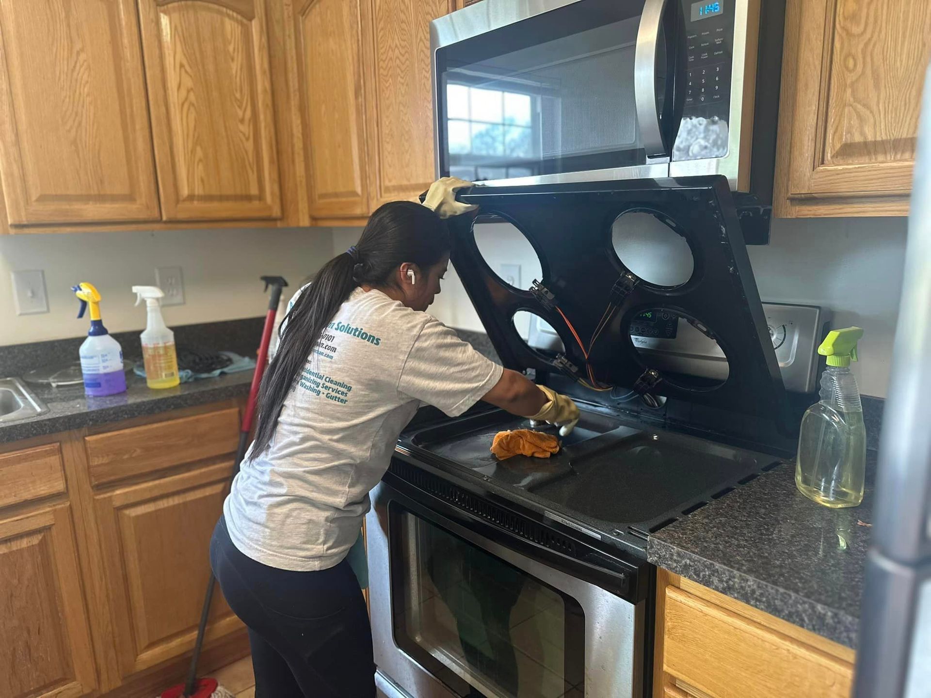 A woman is cleaning a stove in a kitchen.