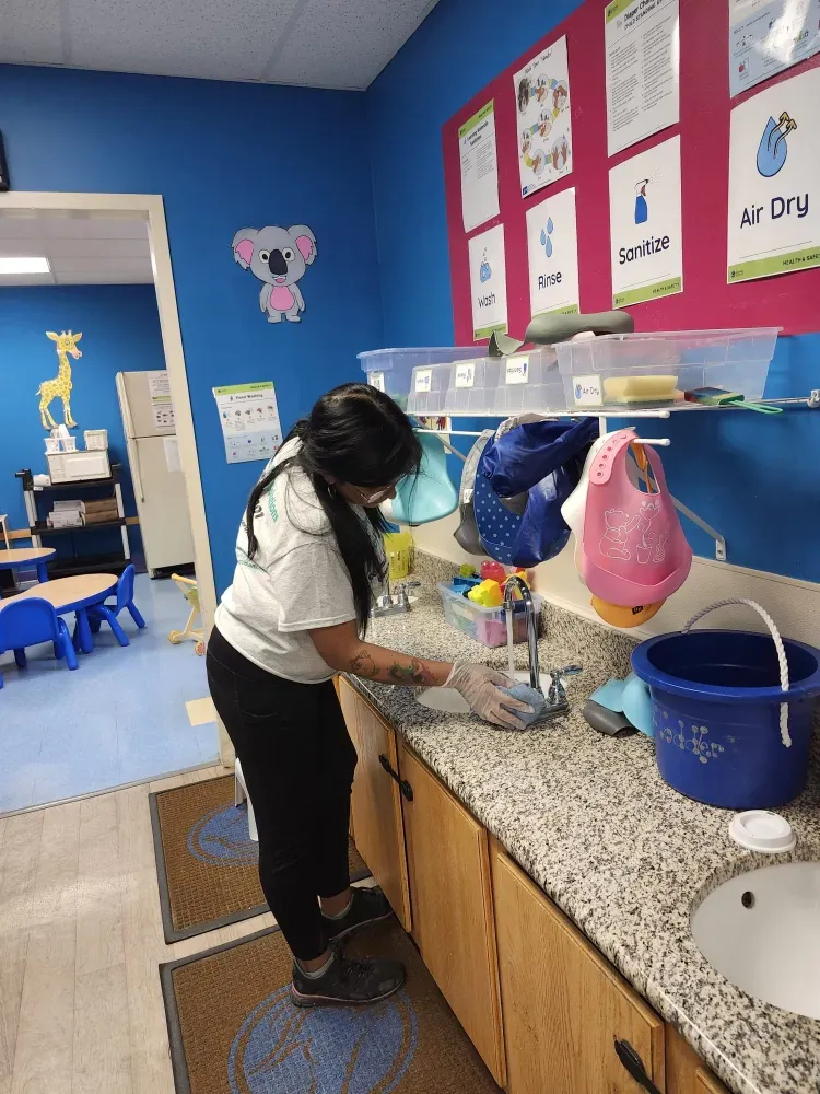 A woman is washing dishes in a kitchen in front of a sink.