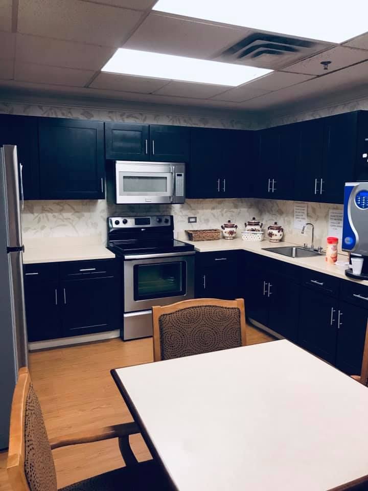 A kitchen with black cabinets , stainless steel appliances , a table and chairs.