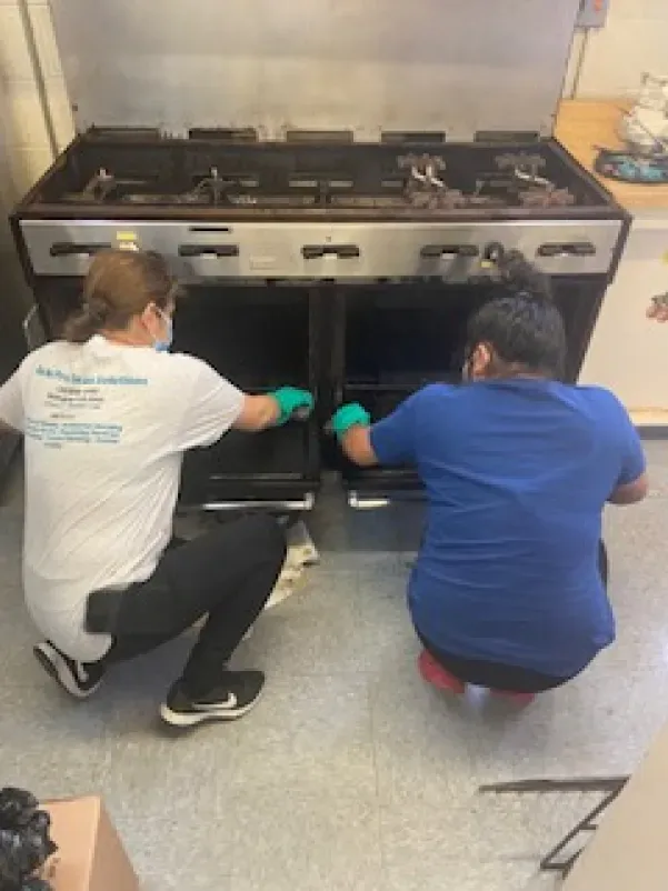 Two women are cleaning an oven in a kitchen.