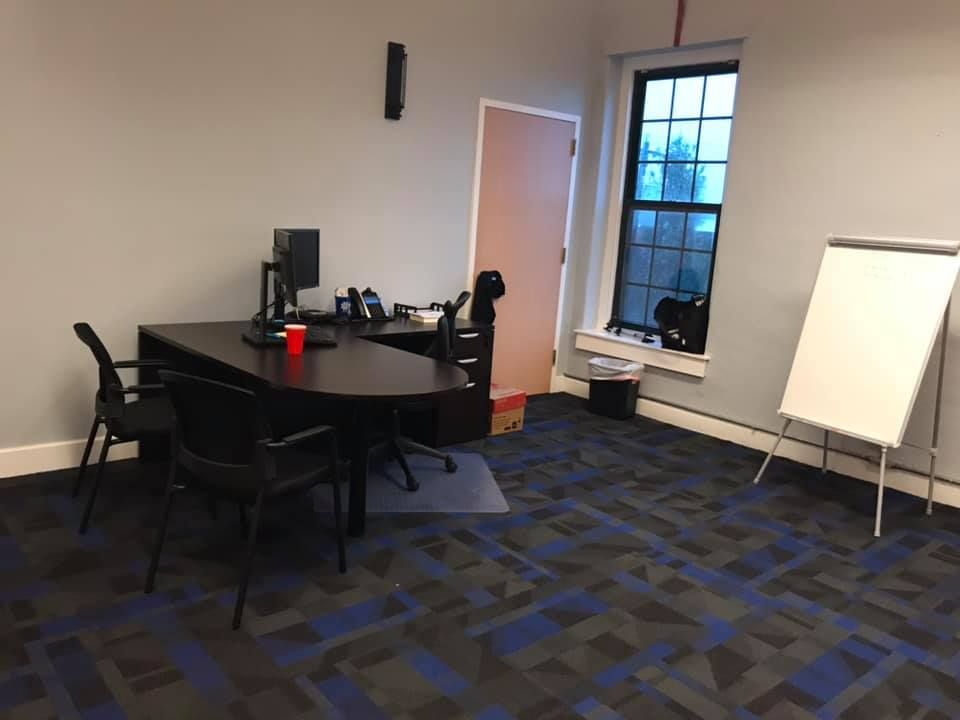 A small office with a desk , chairs , and a whiteboard.