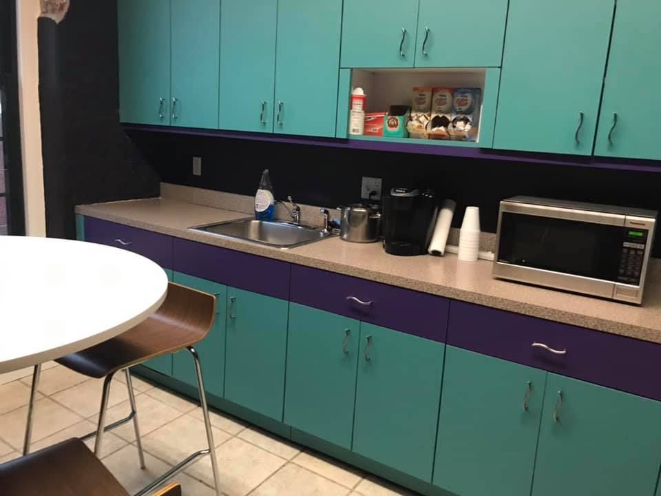 A kitchen with blue cabinets and purple drawers and a microwave