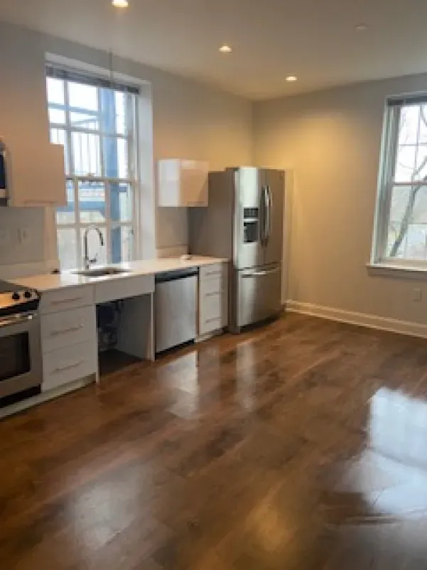 An empty kitchen with stainless steel appliances and hardwood floors