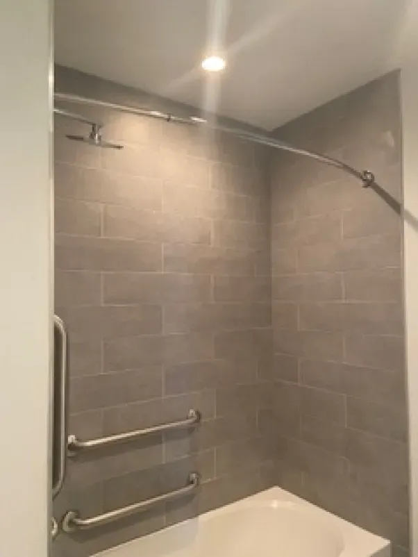 A bathroom with a bathtub and a shower with stainless steel handles.
