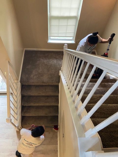 Two people are cleaning the stairs in a house.