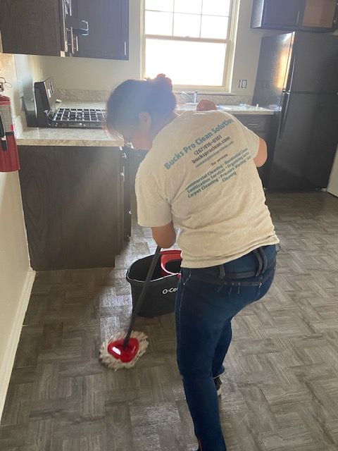A woman is cleaning the floor in a kitchen with a mop and bucket.