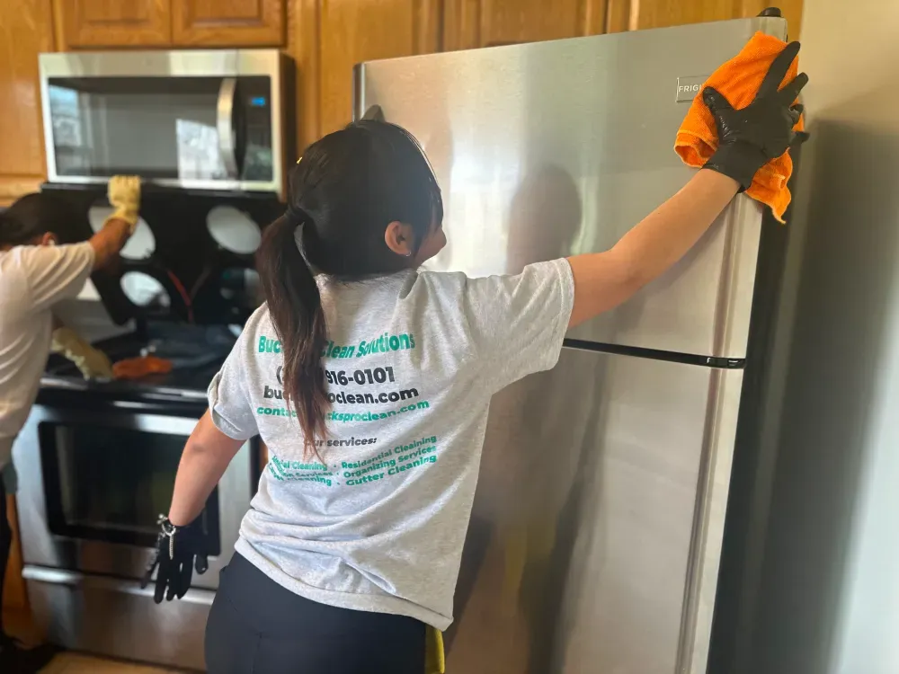 A woman is cleaning a stainless steel refrigerator in a kitchen.