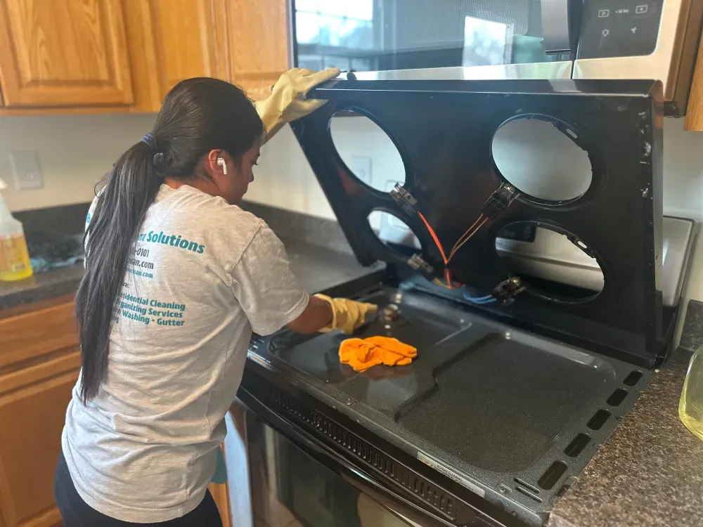 A woman is cleaning a stove top oven in a kitchen.
