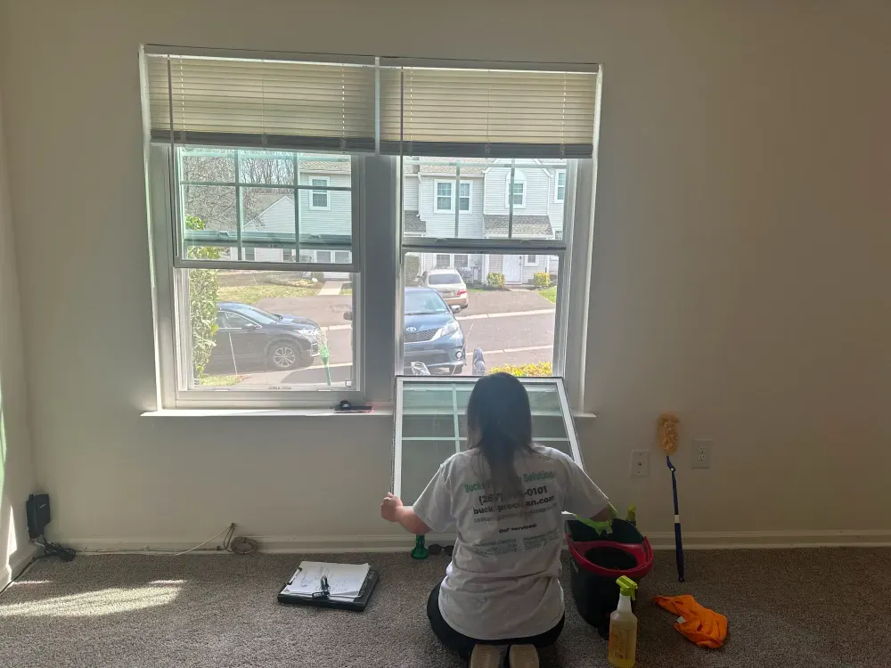 A woman is cleaning a window in an empty room.