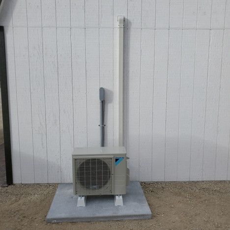 A small air conditioner is sitting on a concrete platform in front of a white wall.