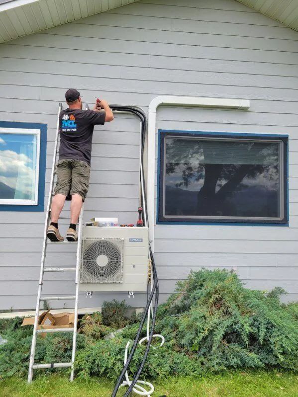 Man installing HVAC unit on a house, working from a ladder. Unit is mounted on a gray siding wall.