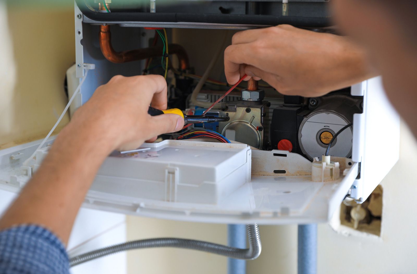 A man is fixing a boiler with a screwdriver.
