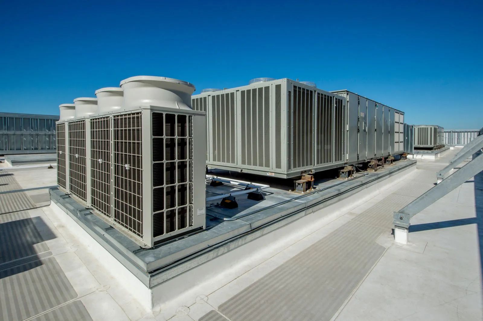 Rooftop HVAC units and industrial equipment on a flat roof under a clear blue sky.