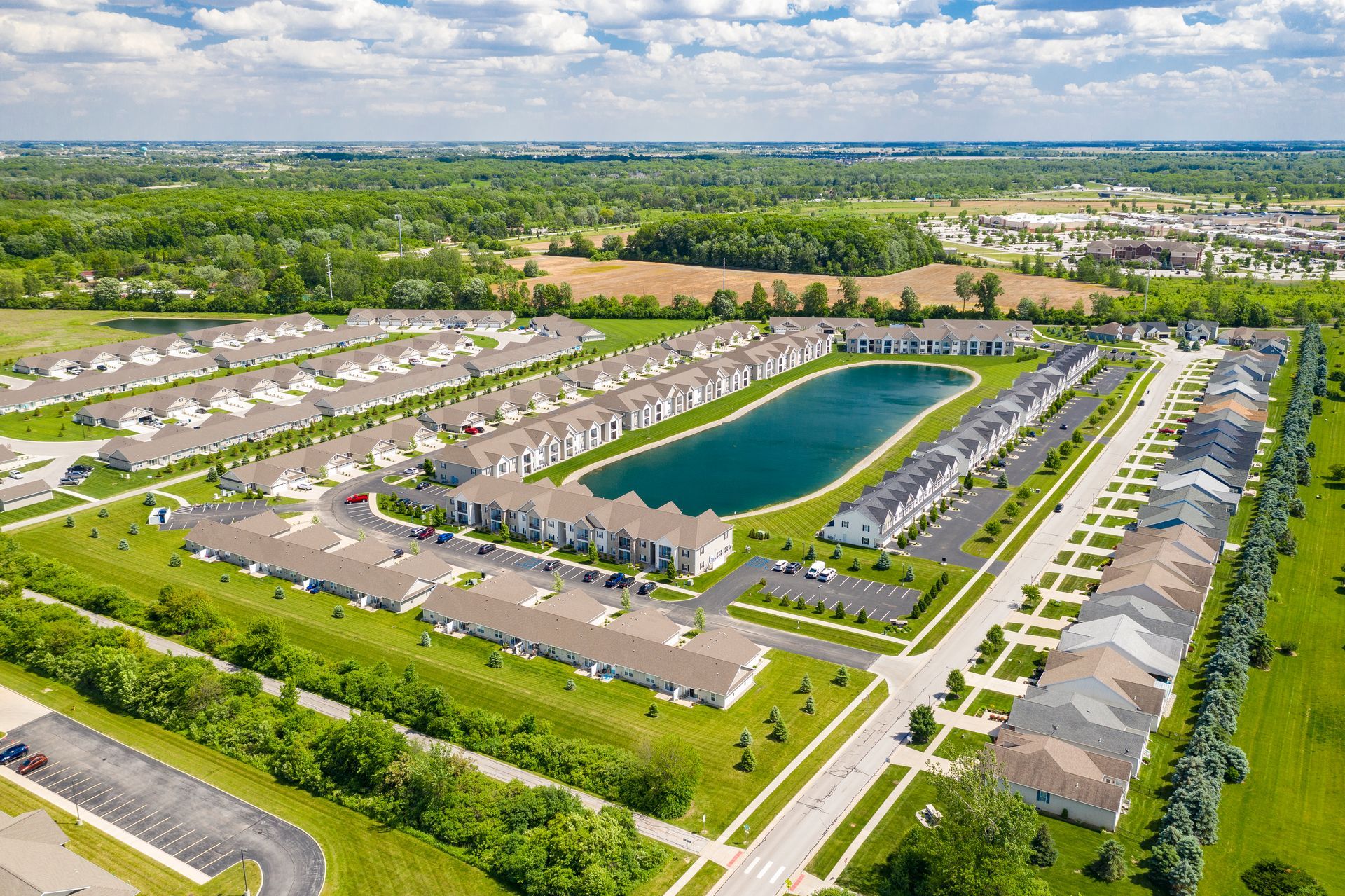 Aerial view of a suburban neighborhood with rows of houses surrounding a lake, trees, and roads.