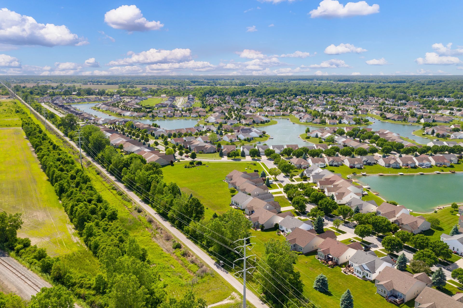 Aerial view of a suburban neighborhood with houses, lakes, and green spaces under a blue sky.