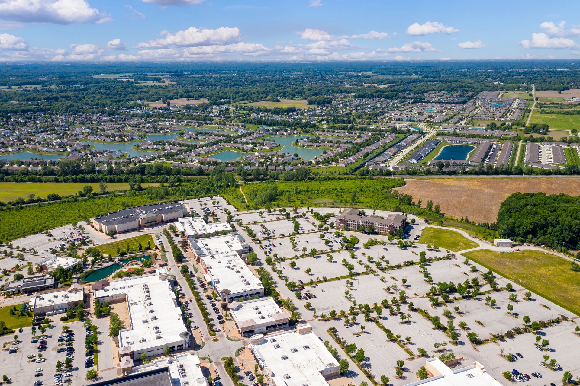Aerial view of a shopping center and adjacent suburban neighborhood under a blue sky.