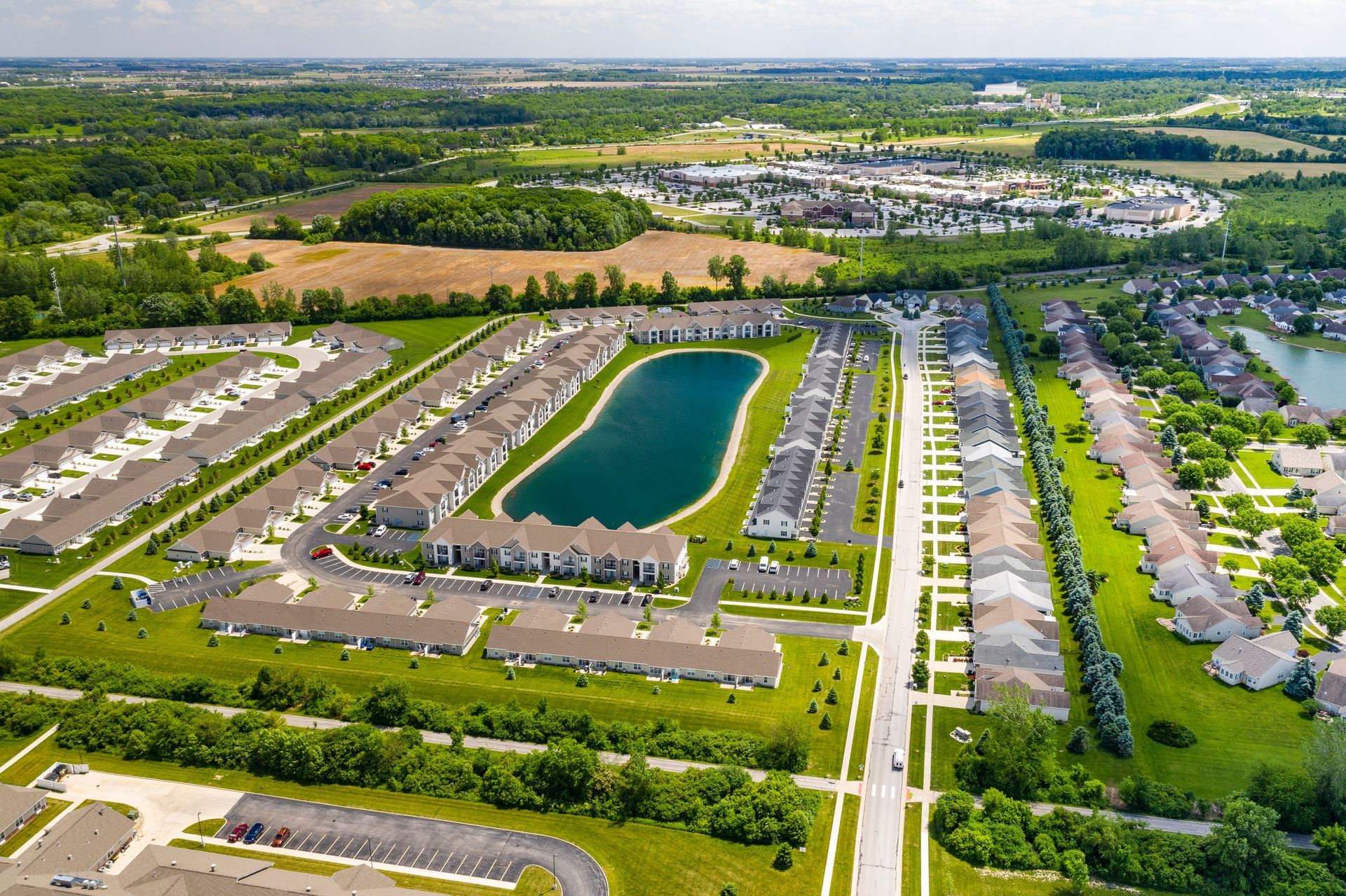Aerial view of a suburban neighborhood with rows of houses, a lake, and green fields.
