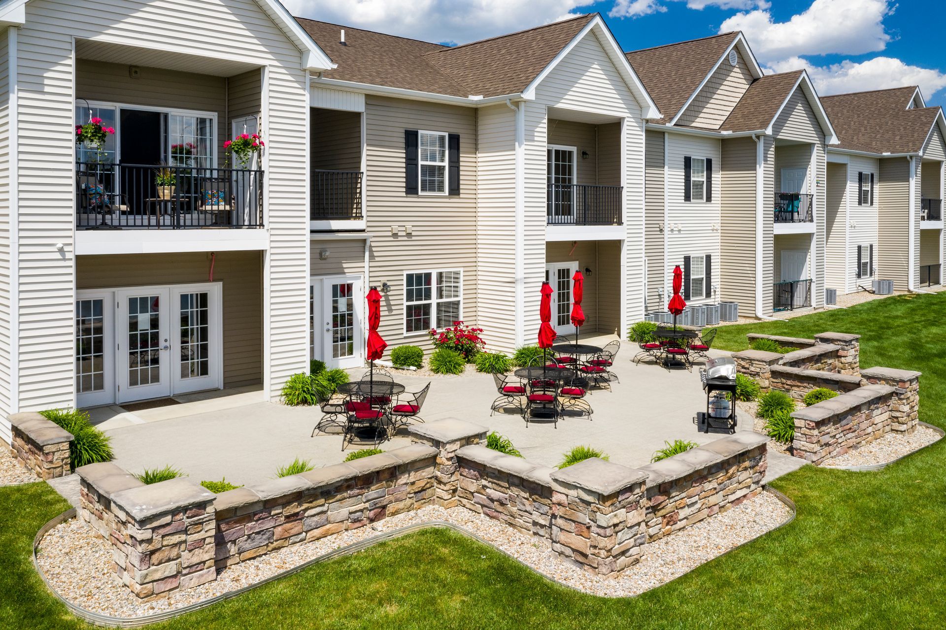 Apartment complex with patio, red umbrellas, and a grassy hill on a sunny day.