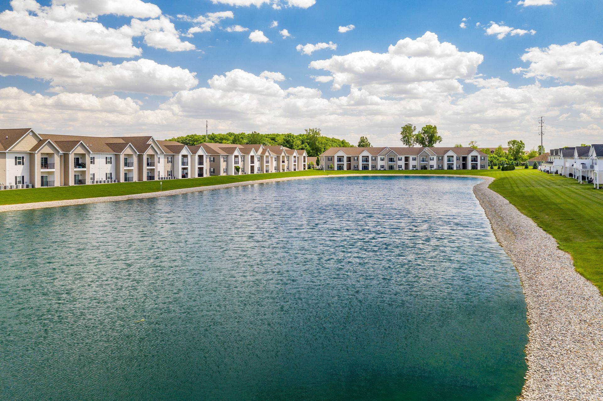 Apartment complex bordering a lake on a sunny day with blue sky and white clouds.