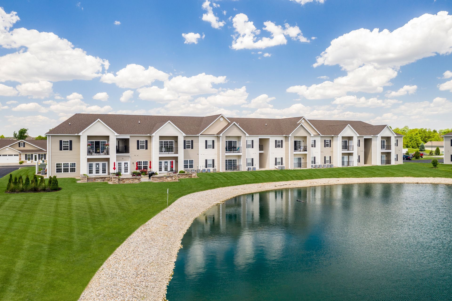Apartment building overlooking a pond on a sunny day with blue sky and white clouds.