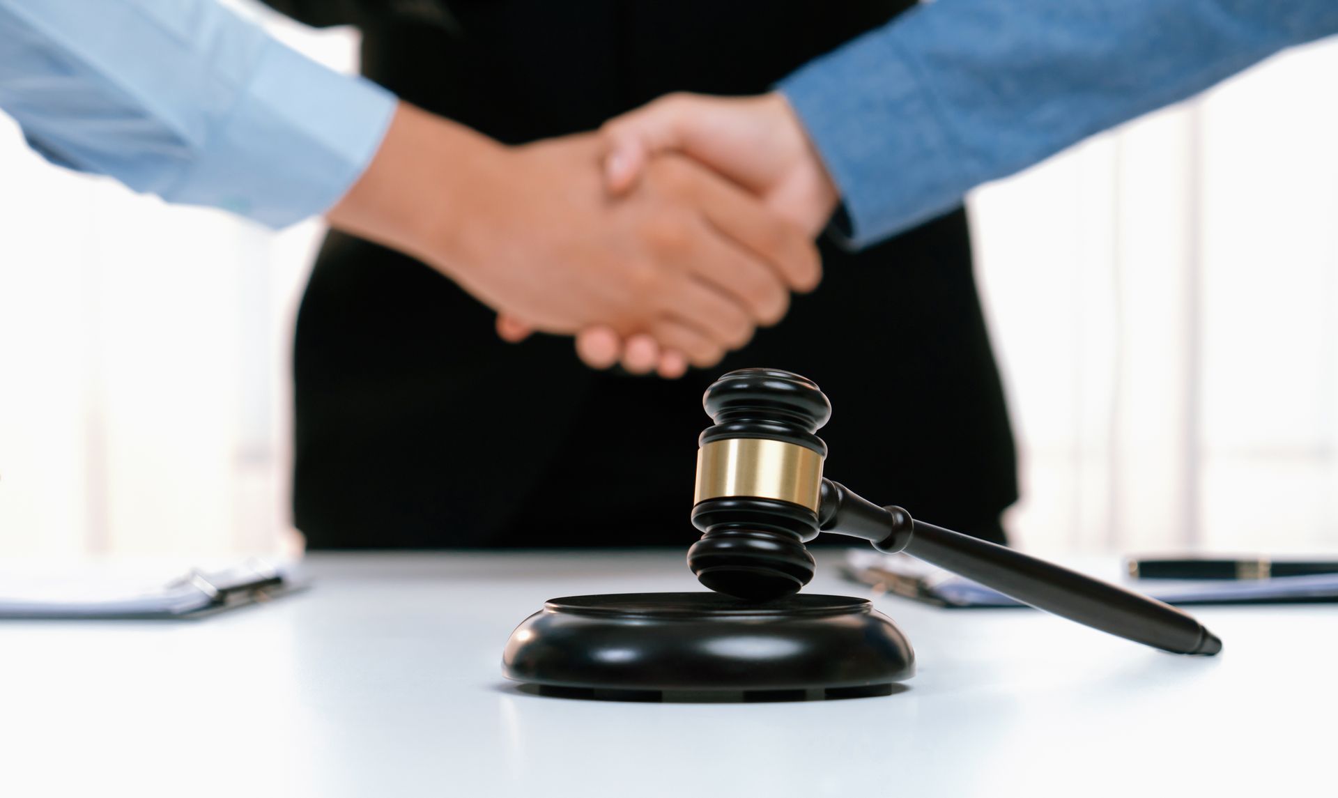 Two people shaking hands, gavel on table.