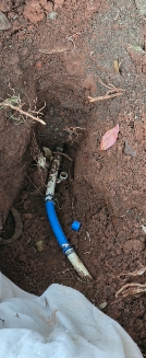 A water pipe in a trench, with a blue and white hose and a blue cap. The surrounding soil is brown.