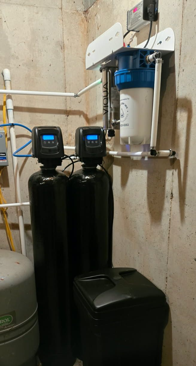 A home water filtration and softening system with two black tanks, a blue canister filter, and a brine tank in a basement.