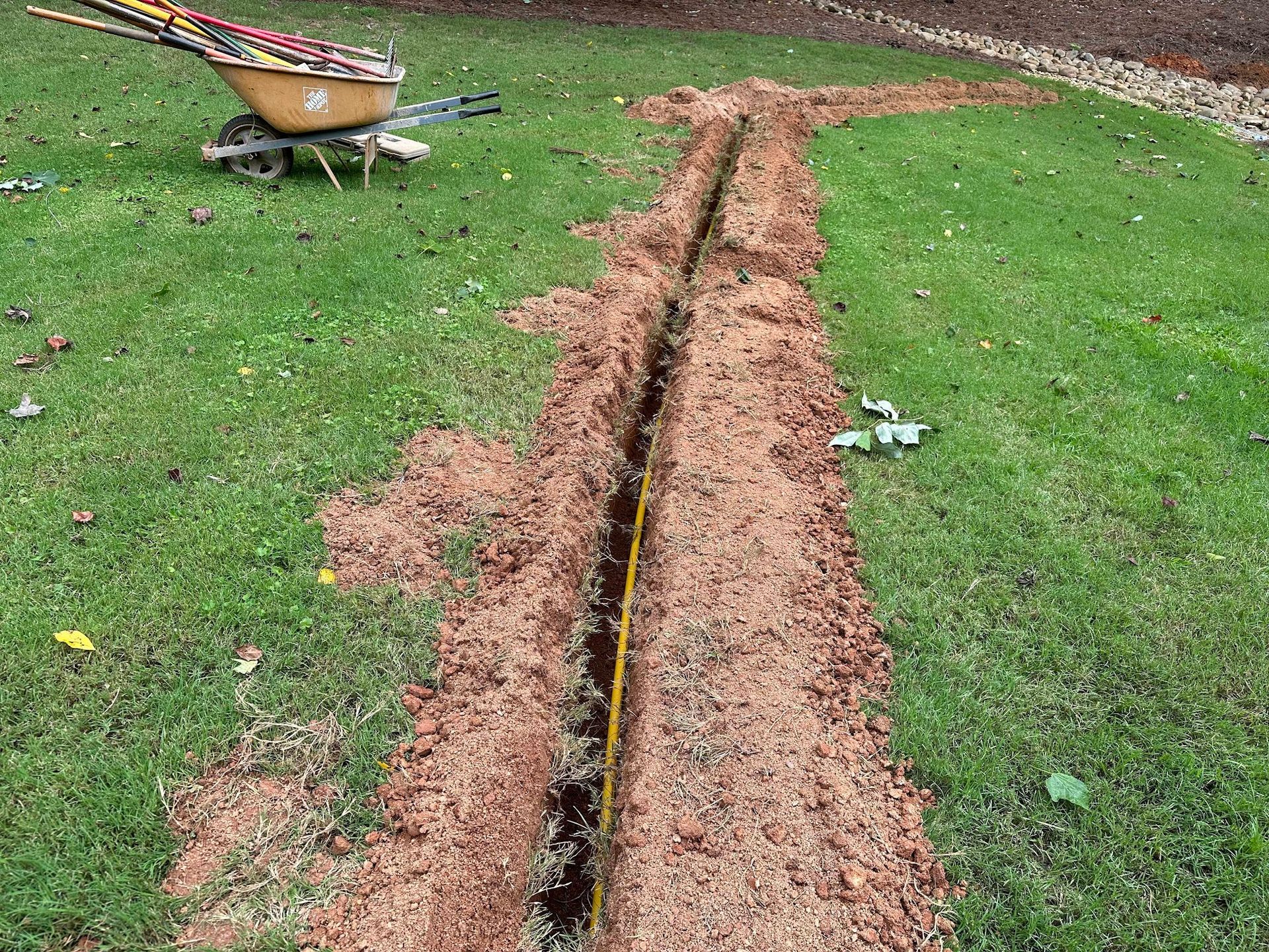 A wheelbarrow is sitting next to a trench in the grass.