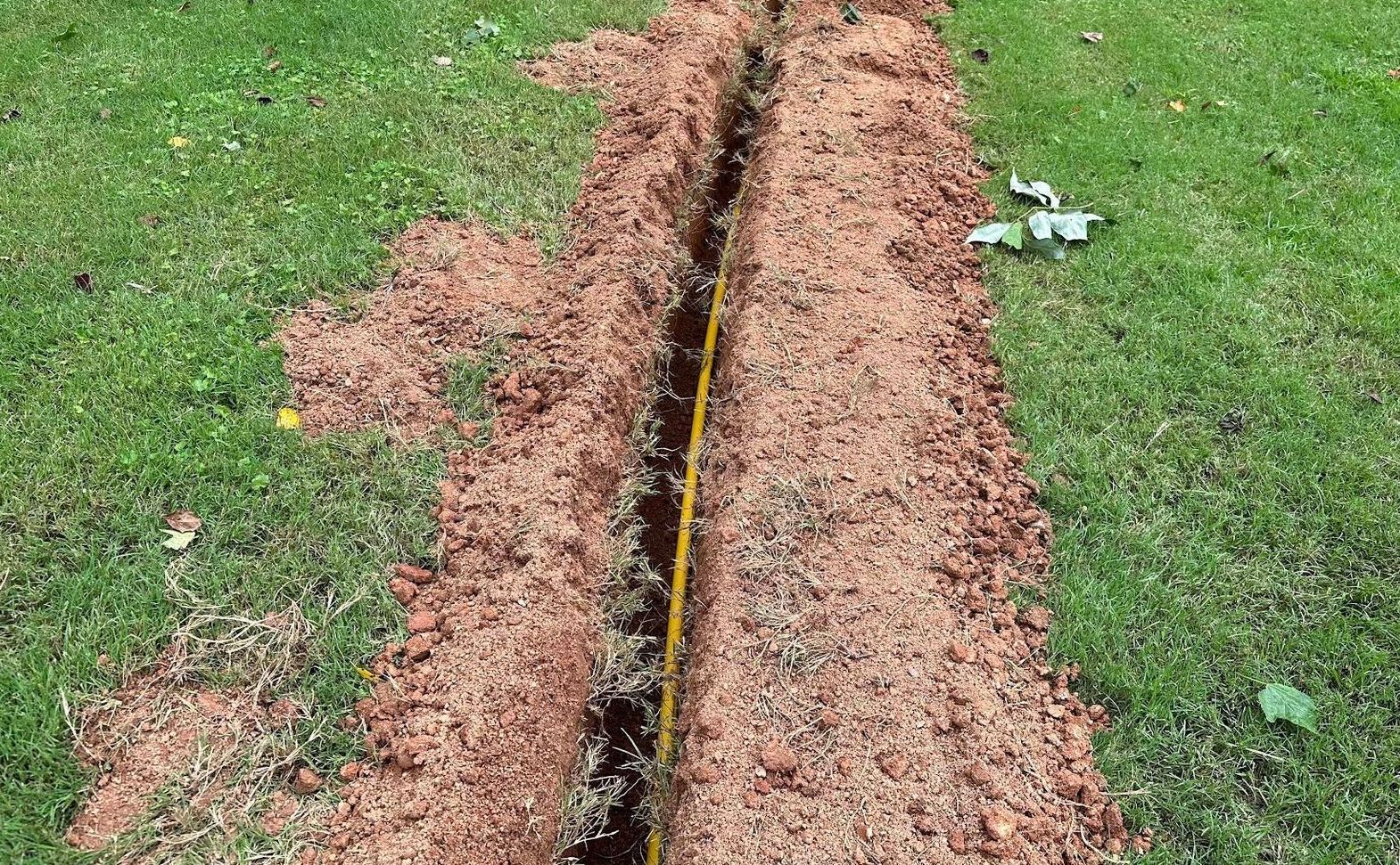 A yellow tape measure is laying in the dirt next to a grassy field.