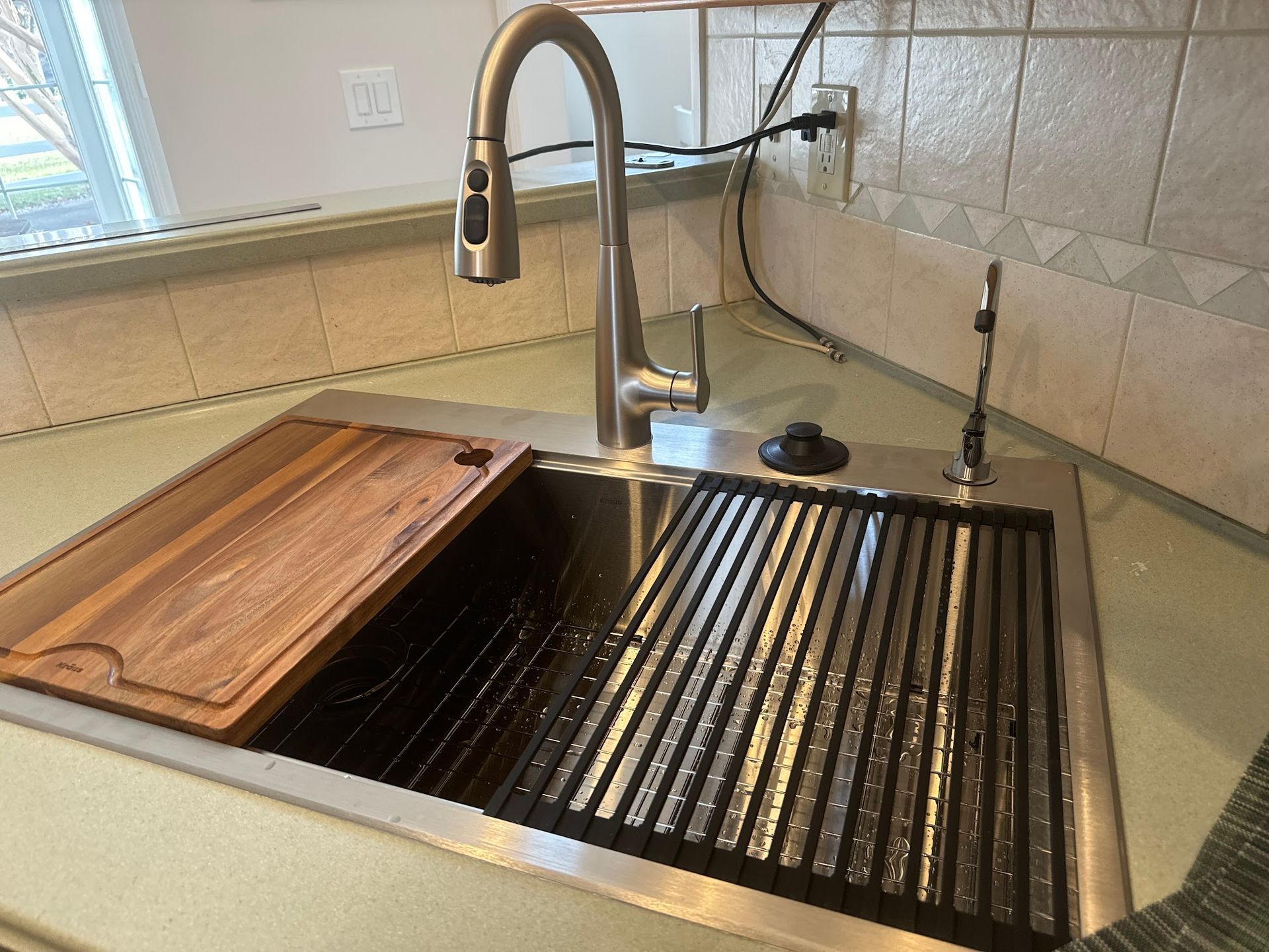 A kitchen sink with a wooden cutting board underneath it