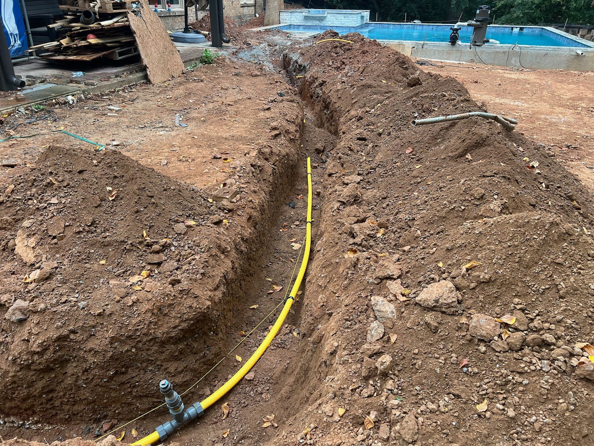 A yellow hose is laying in the dirt next to a pile of dirt.