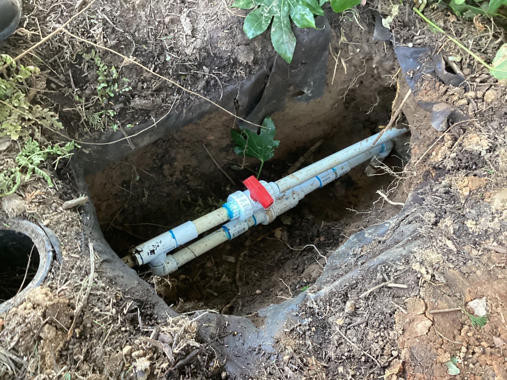 A pipe is laying in the dirt in a hole.