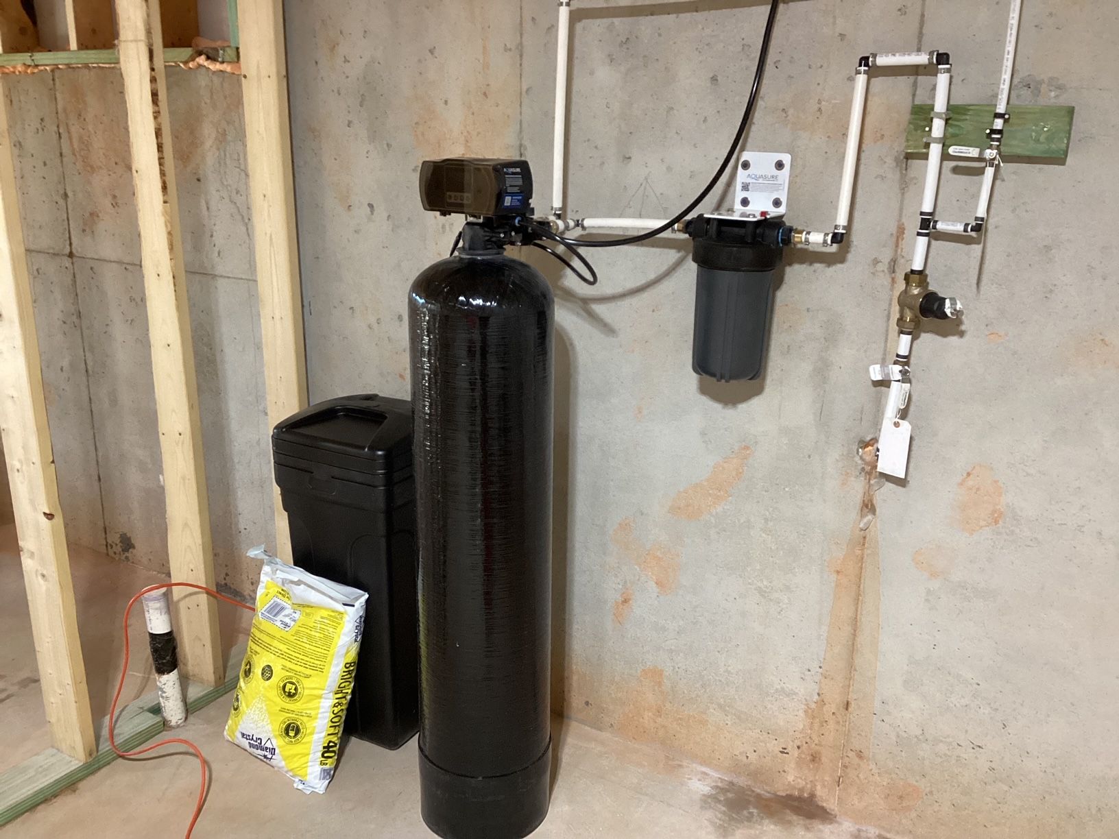A water softener is sitting in a basement next to a wall.