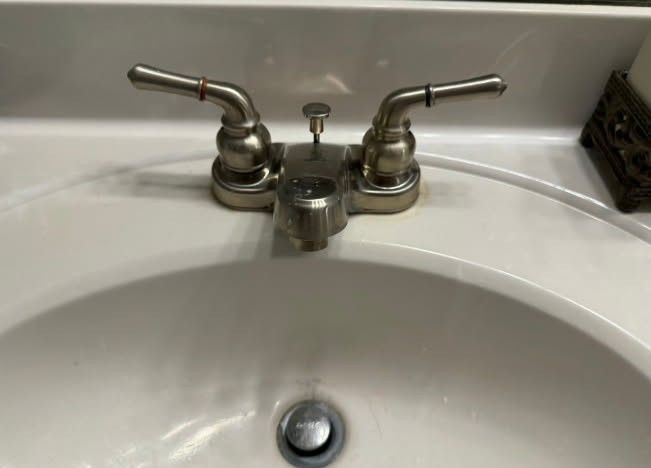 Bathroom sink with dual-handle faucet. White porcelain sink. Faucet is silver with handles slightly angled upwards.