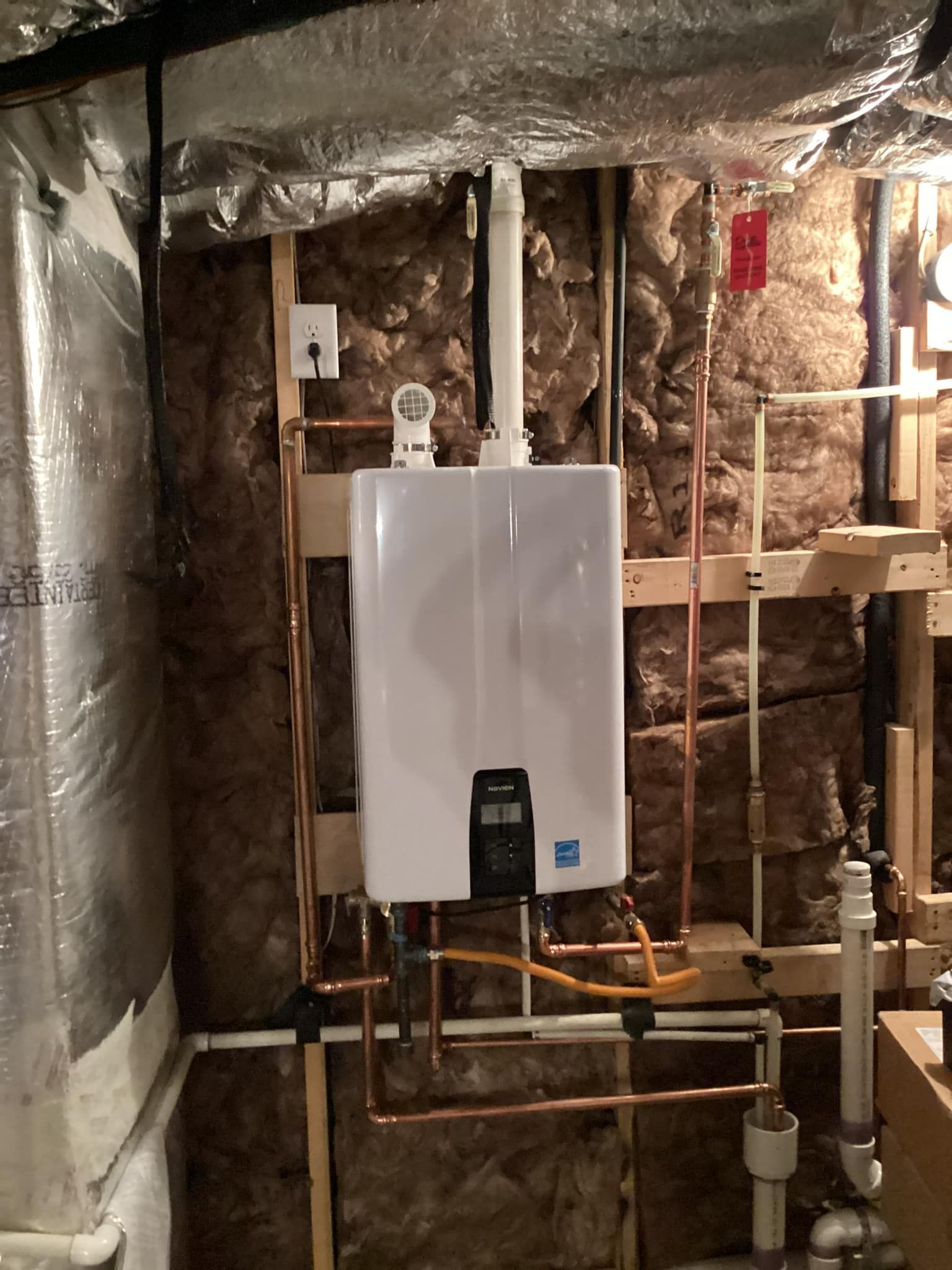 A white water heater is mounted to a wall in a basement.