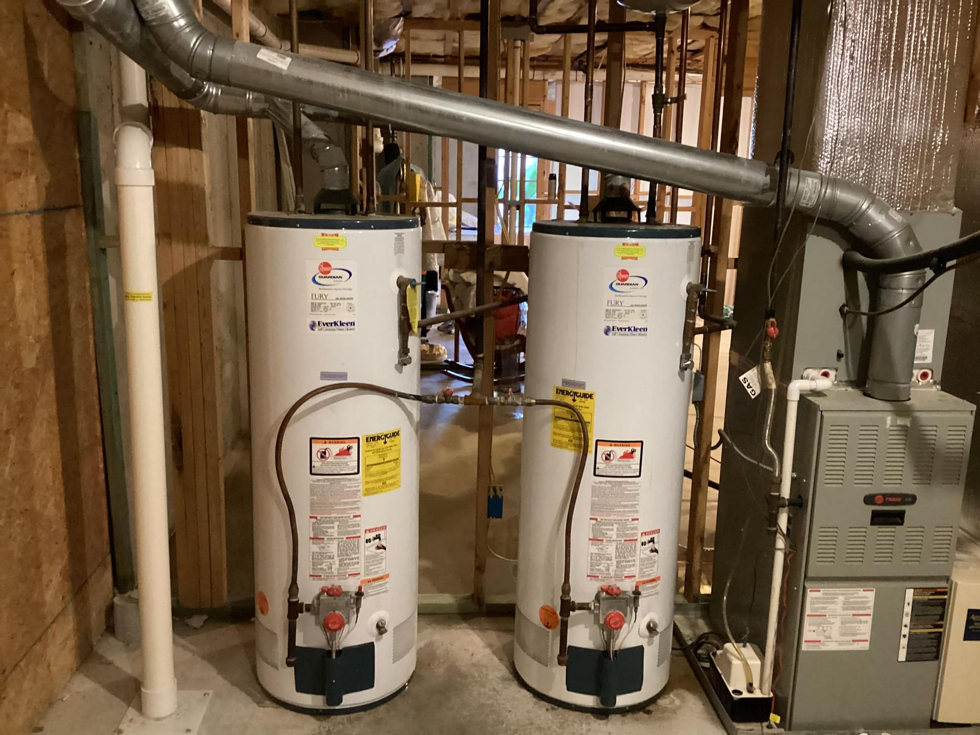Two water heaters are sitting next to each other in a basement.