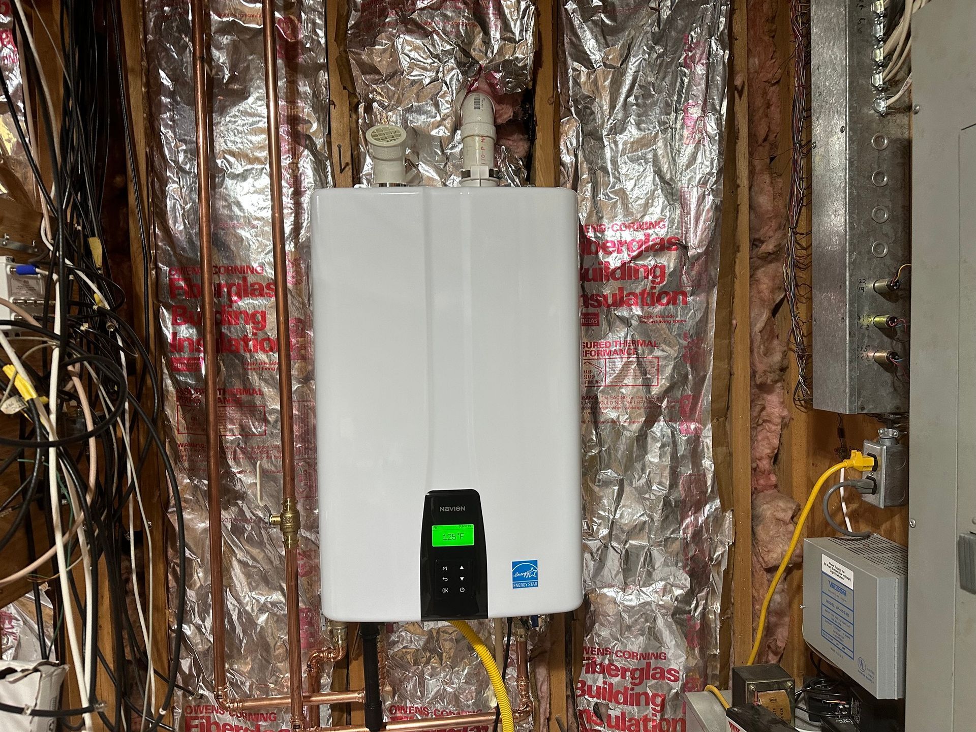 A white water heater is hanging on a wall in a basement.