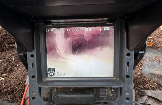 Worker using a sewer camera to inspect a manhole, wearing gloves.