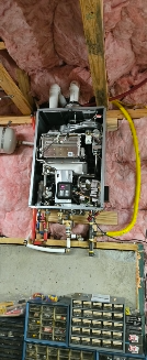 Tankless water heater installed in an insulated attic. Yellow gas line. Pink insulation.