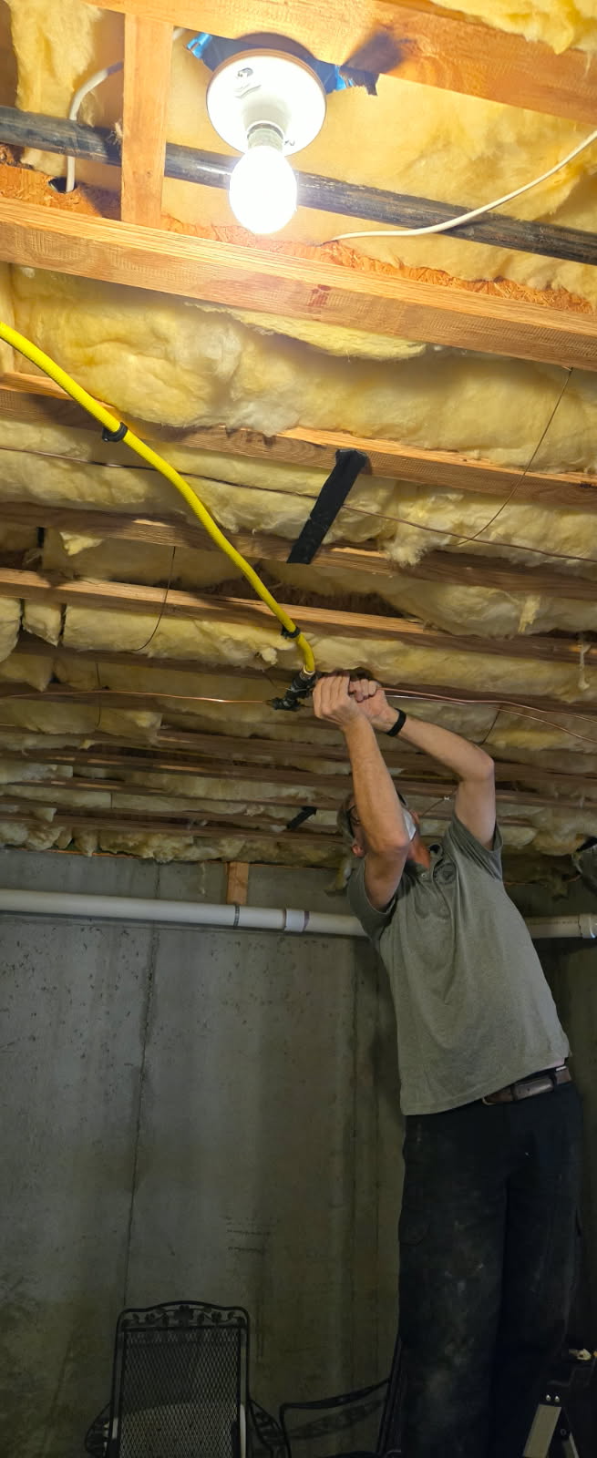 Person in a basement using a yellow tool to work on the ceiling. Light fixture visible.
