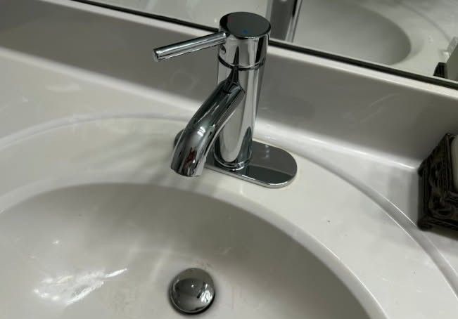 Chrome faucet over a white bathroom sink, viewed from above, with a mirror in the background.