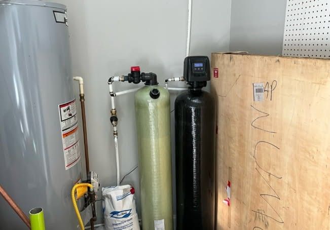 Water softener system next to a water heater in a utility room.
