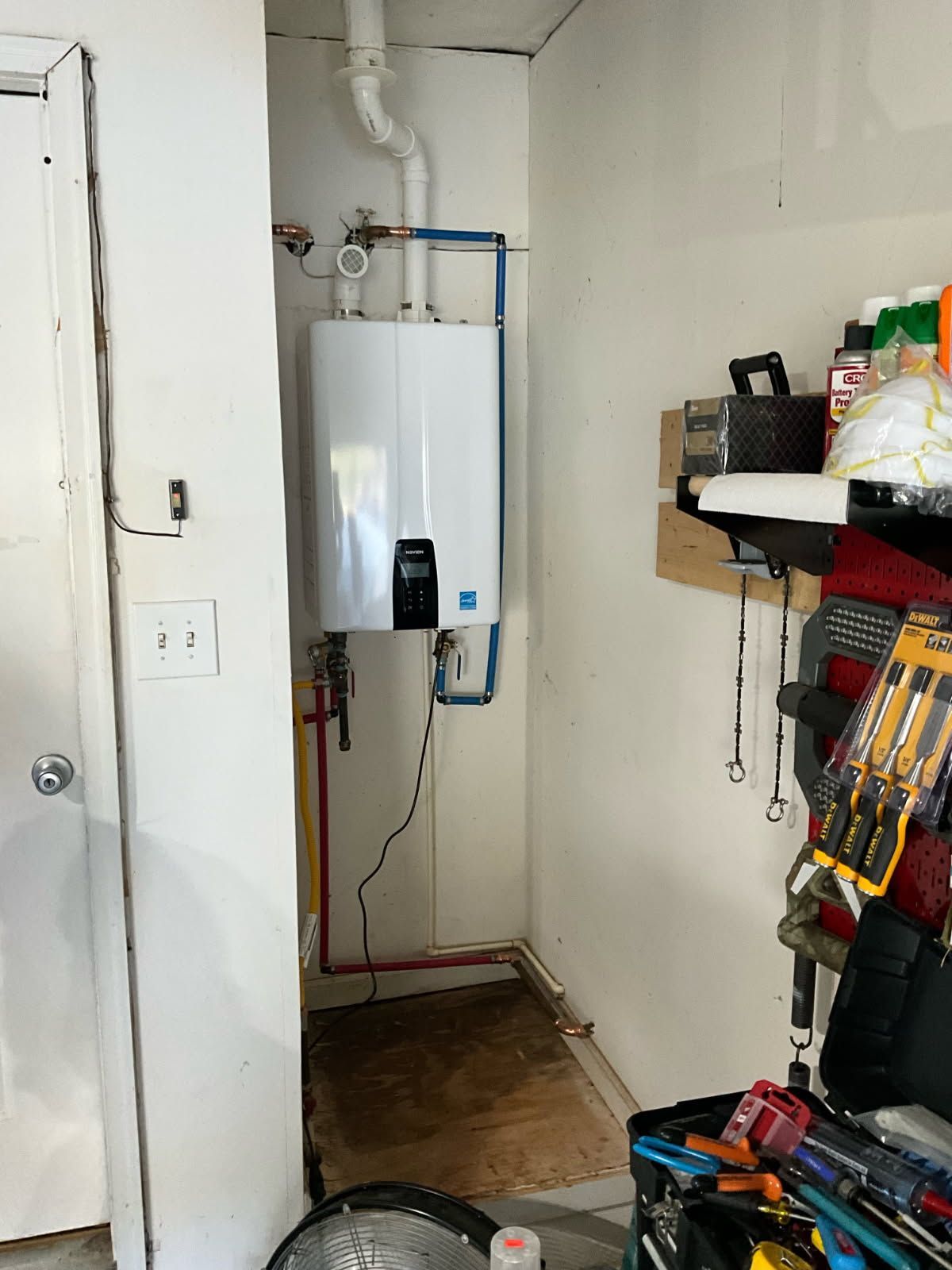 White tankless water heater installed in a garage, with plumbing and electrical connections visible.