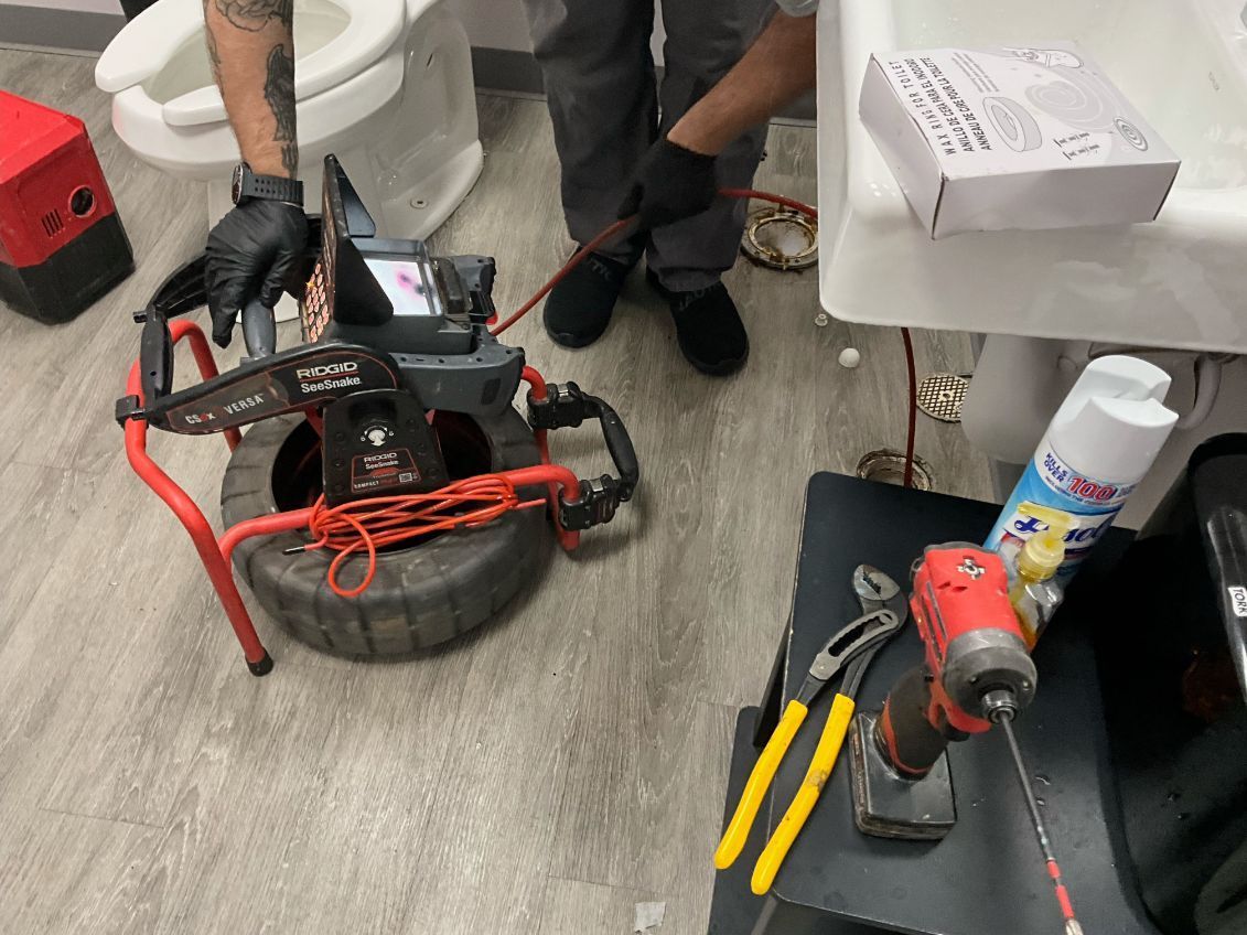 Plumbers using a sewer camera to inspect a drain in a bathroom. Tools and supplies on a table.