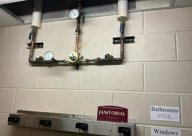 Copper pipes with gauges and valves mounted on a brick wall, labeled 
