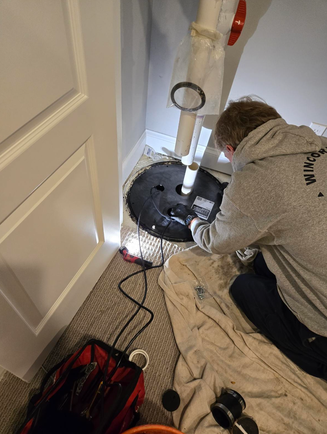 A man is kneeling on the floor working on a sump pump.